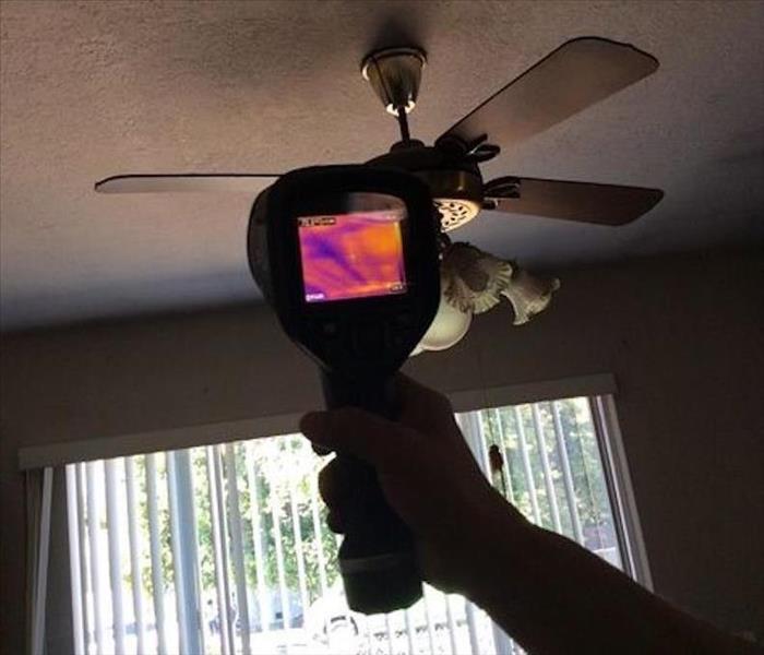 A SERVPRO employee pointing a moisture meter at the ceiling of a home. 
